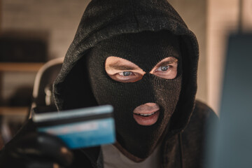 male thief holds a credit card in his hand and picks up a password to steal money. theft from...