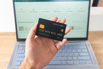 Pov first person holding black mockup credit card for online shop on laptop in home