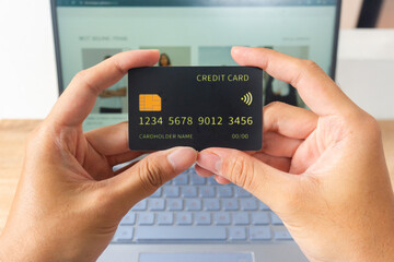 Pov first person holding black mockup credit card with two hands for online shop on laptop in home