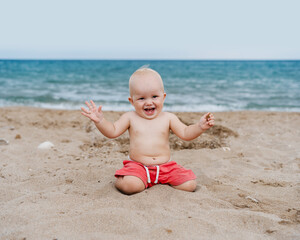 Smiling baby crawling and playing on seaside. Happy little child playing on beach near ocean.