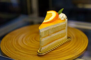 One piece of orange cake topped with orange jam and thinly sliced orange slices, placed on a wooden tray.