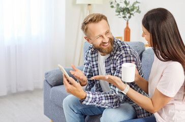 Happy couple at home discussing looking at smartphone screen interested with news, good e-commerce offer, sale, discount, buying ticket via mobile app, funny movie, enjoy together virtual connection