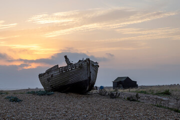 Sunrise over a single beach: Fishing boats rest on the shingle beach, bathed in the warm glow of the morning light, as the serene coastal landscape awakens