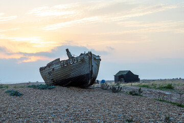 Sunrise over a single beach: Fishing boats rest on the shingle beach, bathed in the warm glow of the morning light, as the serene coastal landscape awakens