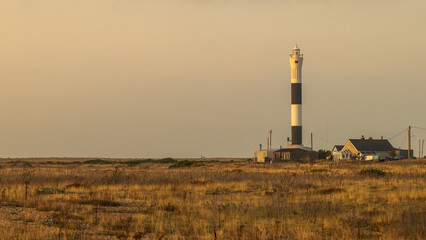 Sunrise over a single beach: Fishing boats rest on the shingle beach, bathed in the warm glow of the morning light, as the serene coastal landscape awakens
