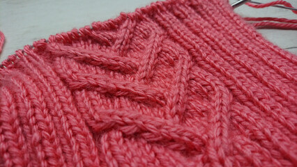Close-up of pink knitted fabric with braided cable pattern. Detailed photography of hand-knitting texture. Crafting and handmade design concept for textile and print
