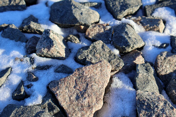Close-up of stones covered with snow on the ground. Textured rock surface with white snow in winter season. Nature and outdoor landscape concept for design and print