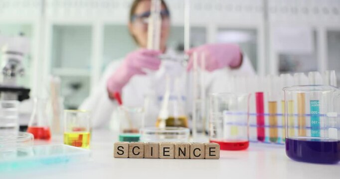 Wooden cubes form word SCIENCE on laboratory table. Woman lab technician prepares necessary equipment for scientific experiment. Slow motion