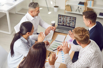 Coworkers working together in an office while participating in a group online video call. People team focuses on business tasks, ensuring effective communication during the virtual meeting.