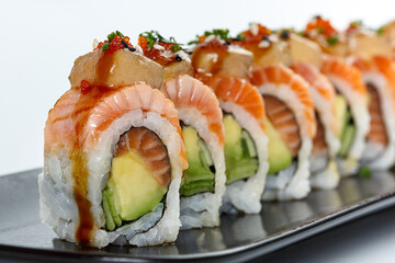 A beautifully plated sushi roll with layers of fresh salmon, avocado, cucumber, and rice, topped with foie gras, fish roe, and drizzled with savory sauce for a gourmet experience