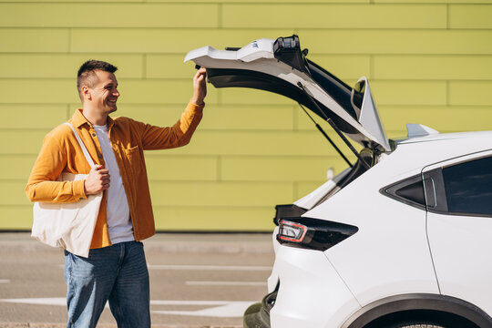 Smiling man opening trunk of car while shopping in the city, holding shopping bag
