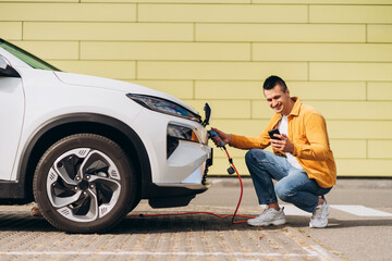 Young man using mobile phone app online for charging his electric car