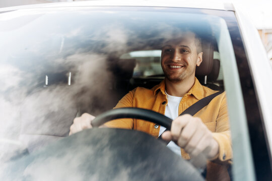Handsome young man is smiling while sitting in his new car