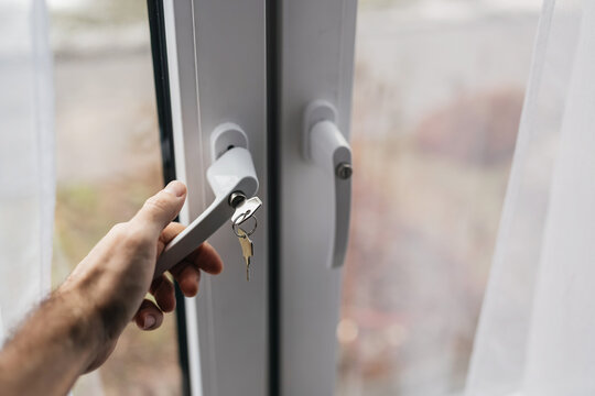 Male hand holding window handle to street with locking key for child safety.