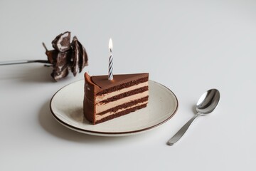 Chocolate layered cake slice with a burning candle