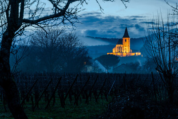 Église mixte d’Hunawihr au crépuscule : au pied du vignoble, sous un ciel nocturne bleu nuit après une pluie d’hiver, CEA, Alsace, Grand Est, France