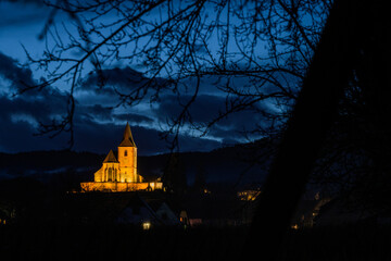 Hunawihr, au crépuscule : l’église mixte se détache dans le ciel nocturne bleu nuit, après une pluie d’hiver, CEA, Alsace, Grand Est, France