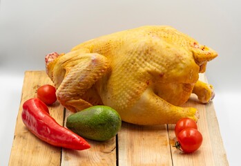 Fresh raw whole chicken with lemon and vegetables on a wooden cutting board on a white background. Healthy eating, diet and cooking.