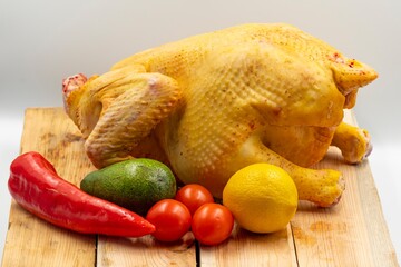 Fresh raw whole chicken with lemon and vegetables on a wooden cutting board on a white background. Healthy eating, diet and cooking.