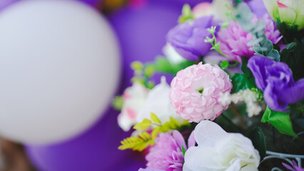 A vibrant arrangement of colorful flowers, complemented by a white balloon and purple backdrop, creating a festive atmosphere.