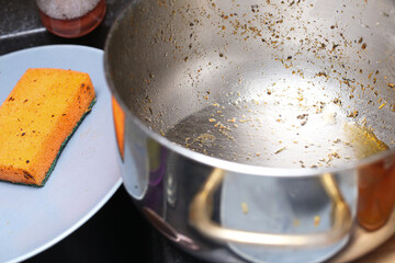 Dirty greasy metal pot with sponge for dishwashing. Cleaning tasks kitchen interior. Stubborn stains removal. Household chores background. Removing difficult grime and restoring shine.