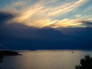 A serene coastal landscape featuring dramatic clouds, calm ocean waters, a small island, and a lone sailboat on the horizon. The scene evokes feelings of tranquility, exploration