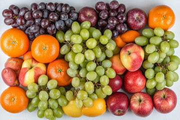 Colorful arrangement of assorted fruits including oranges, grapes, apples, and lemons on a light background 
