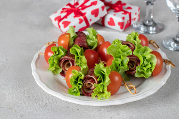 Canape with sausage, cheese, cherry tomatoes and lettuce leaves on white plate, snack for Valentines Day