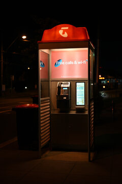 Illuminated Telstra payphone beside a road at night, featuring signage promoting free phone calls and wi-fi