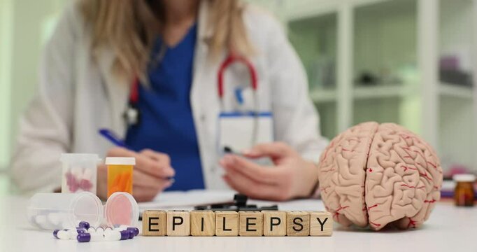 Word Epilepsy with drugs and human brain model on doctor desk. Professional neurologist discusses disease treatment with patient in clinic
