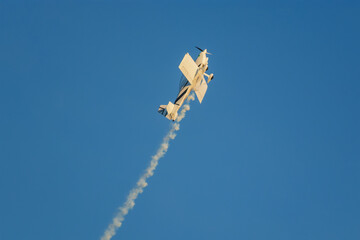 Stunt aerobatic plane performing stunts in blue sky with smoke trail. Concept of speed, difficulty,...