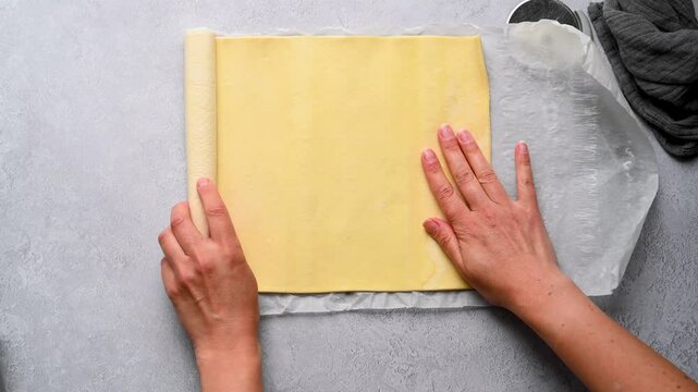 Female hands rolling raw puff pastry dough with hands on the table. Cooking puff pastry pies