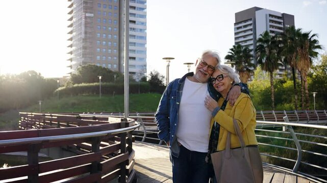 Happy adult Caucasian elder couple stroll embraced walking for park the in city. Retired mature people in love enjoying romantic getaway. Positive relationships and spring retiree holidays