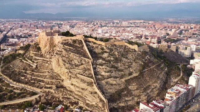ALicante city, Spain. Castle of Santa B&aacute;rbara on top of the hill. Drone going backwards. View of promenade of Alicante and Postiguet Beach. Famous travel destination. Sunset point. Orange reflections.