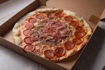 Pizza na caixa de papelão com queijo mozarela e vários sabores e condimentos, feita de massa fina, farinha
