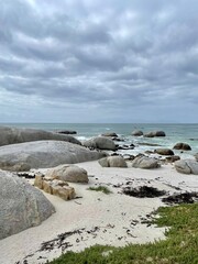 A serene coastal landscape with large rocks scattered across the white sandy shoreline, set against a dramatic cloudy sky. Ideal for nature and travel themes.