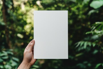 A person holds a blank sheet of paper against a lush, green natural backdrop.