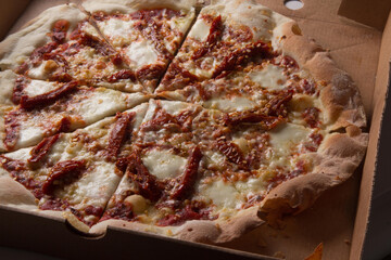 Pizza na caixa de papel&atilde;o com queijo mozarela e v&aacute;rios sabores e condimentos, feita de massa fina, farinha