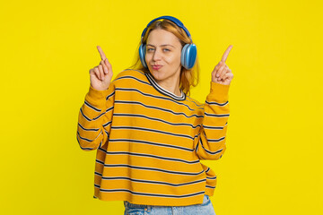 Happy joyful Caucasian woman in blouse listening music on headphones and dancing disco fooling...