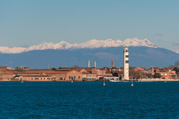 Fototapeta premium Panorama dell’isola di Murano e del suo faro con le Dolomiti coperte di neve sullo sfondo, in una giornata invernale
