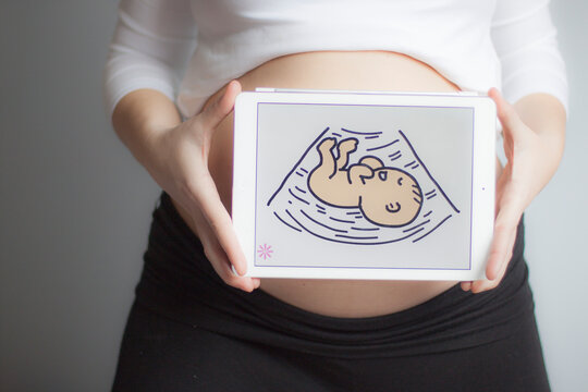 Close-up of a Pregnant woman holding a digital tablet with a picture of a baby in front of her abdomen