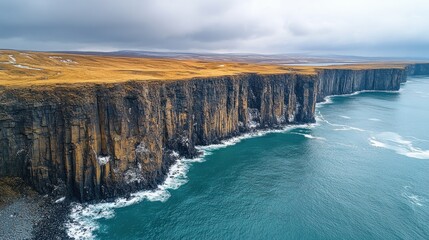 Aerial view of dramatic cliffs meeting the ocean, showcasing rugged landscape under a cloudy sky