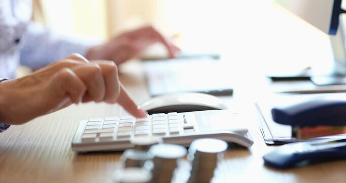 A focused individual diligently using a calculator while handling various coins on a wellorganized workspace