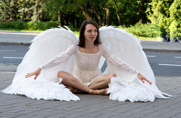 A girl in a white dress and with large white wings sits on the asphalt