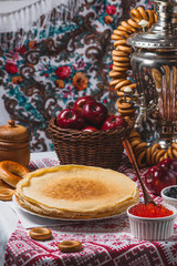 Pancakes on the table with traditional patterns, next to the samovar, apples and caviar
