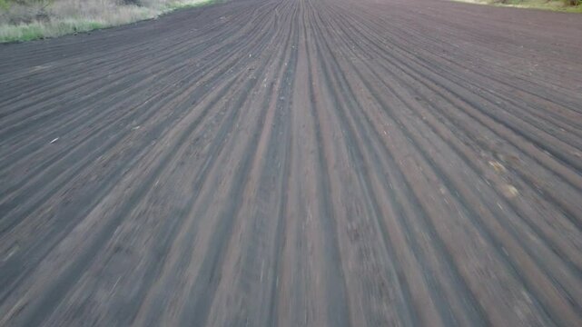 Drone flyover of a freshly plowed field with parallel rows of soil.