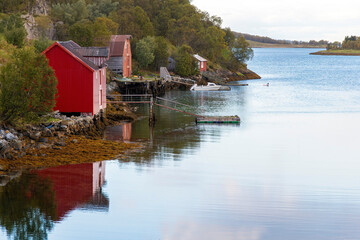Obraz premium Tranquil water of a fjord on the Lofoten island chain in Norway with traditional red fisherman cabins (rorbu) along the shore reflected in water