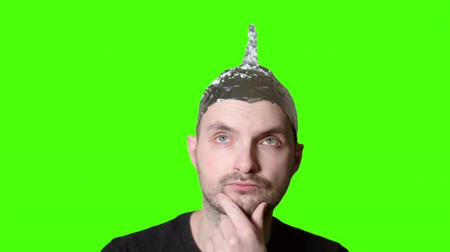 Man wearing tin foil hat on green screen background is thinking