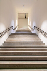 Low angle view of brightly lit white colored contemporary concrete stairwell or staircase with modern handrails on both sides