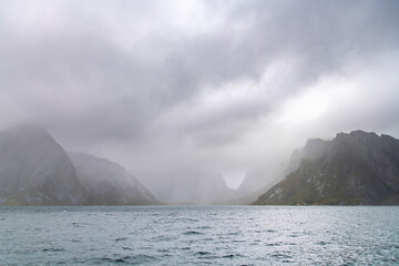 Dramatic cloudscape with dark cloud cover over silhouette mountain range in water of fjord on Lofoten island chain archipelago near Reine, Norway
